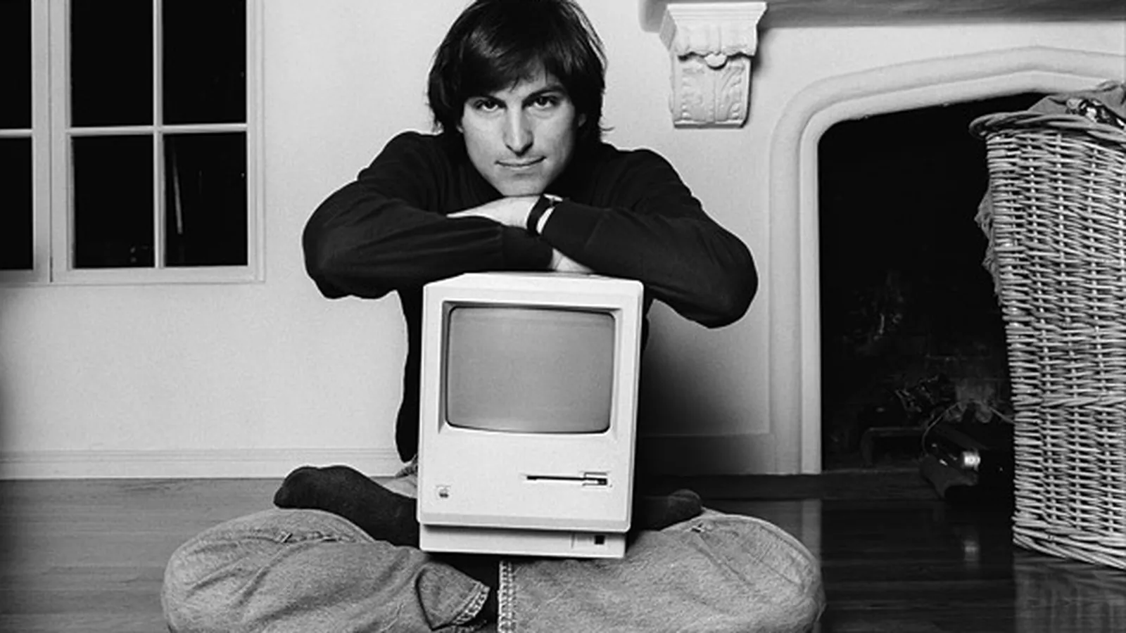 Steve Jobs sentado com o primeiro Macintosh nas pernas