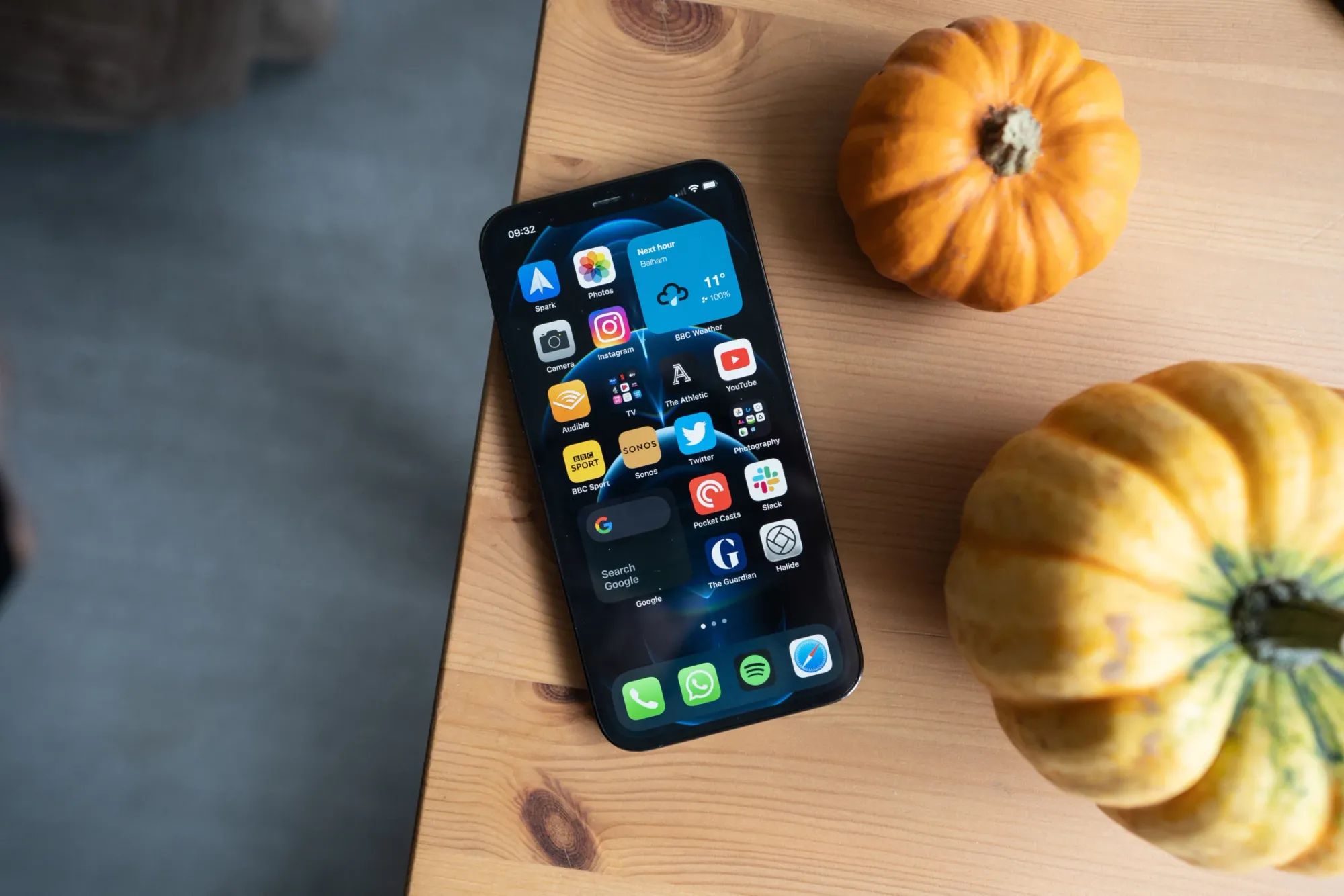 Vista de cima de um iPhone numa mesa de madeira com duas abóboras à direita, uma mais pequena, acima e, uma maior, abaixo. 